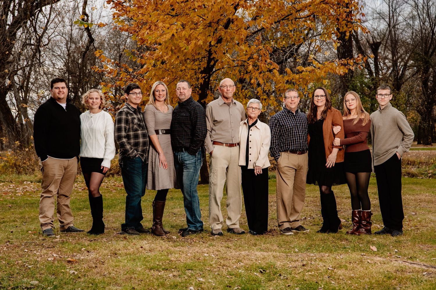 A group of people wearing coordinated beige and brown outfits pose together outdoors during autumn.