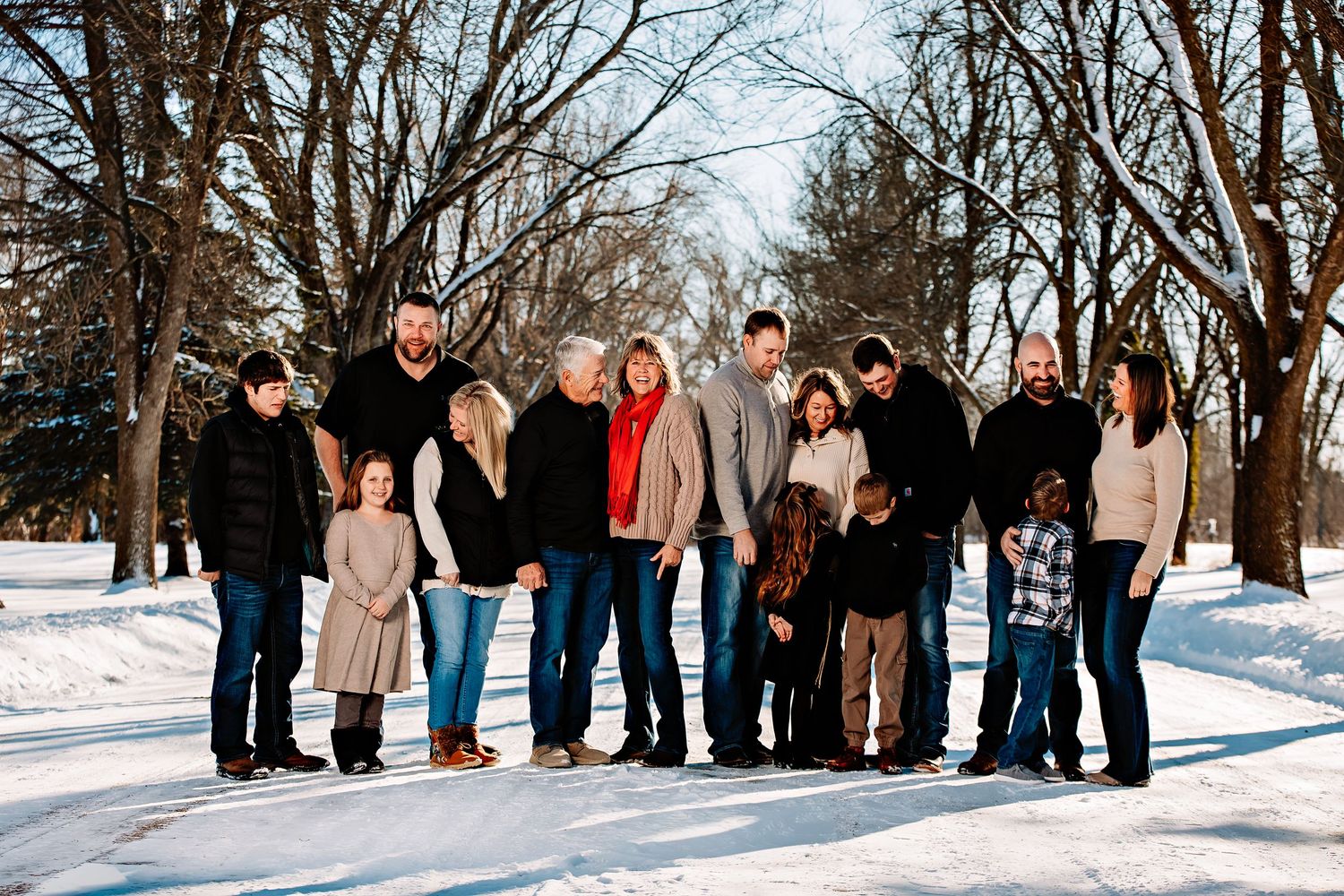 A large family group poses together on a snowy winter path lined with bare trees.