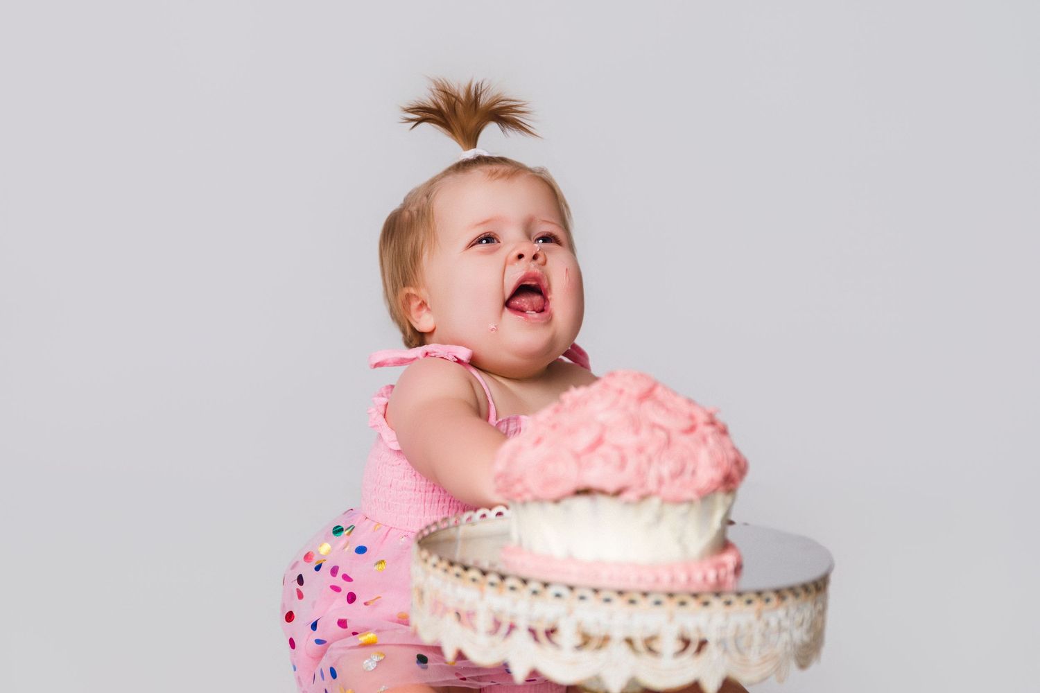 Close-up shots of baby reacting to pink birthday cake during smash cake session.