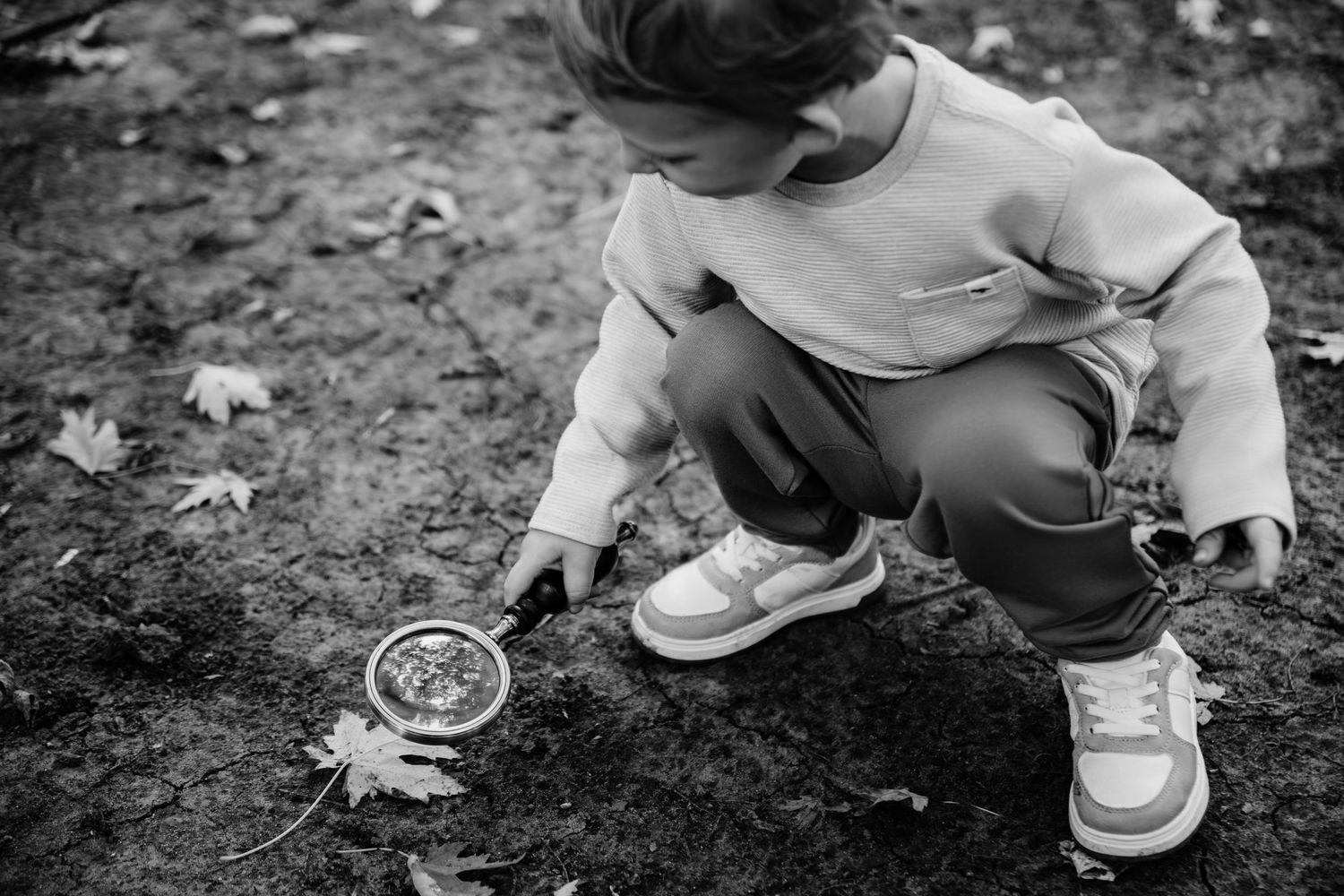 A child in light colored clothing crouches down to examine something on the ground in black and white.