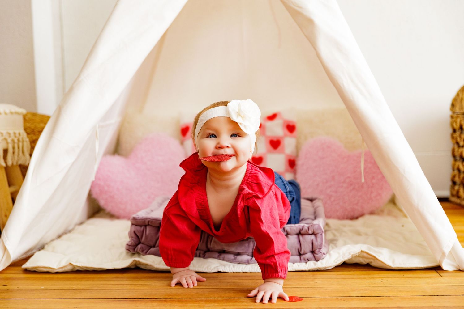 Child playing inside a white teepee tent decorated with red heart garlands.
