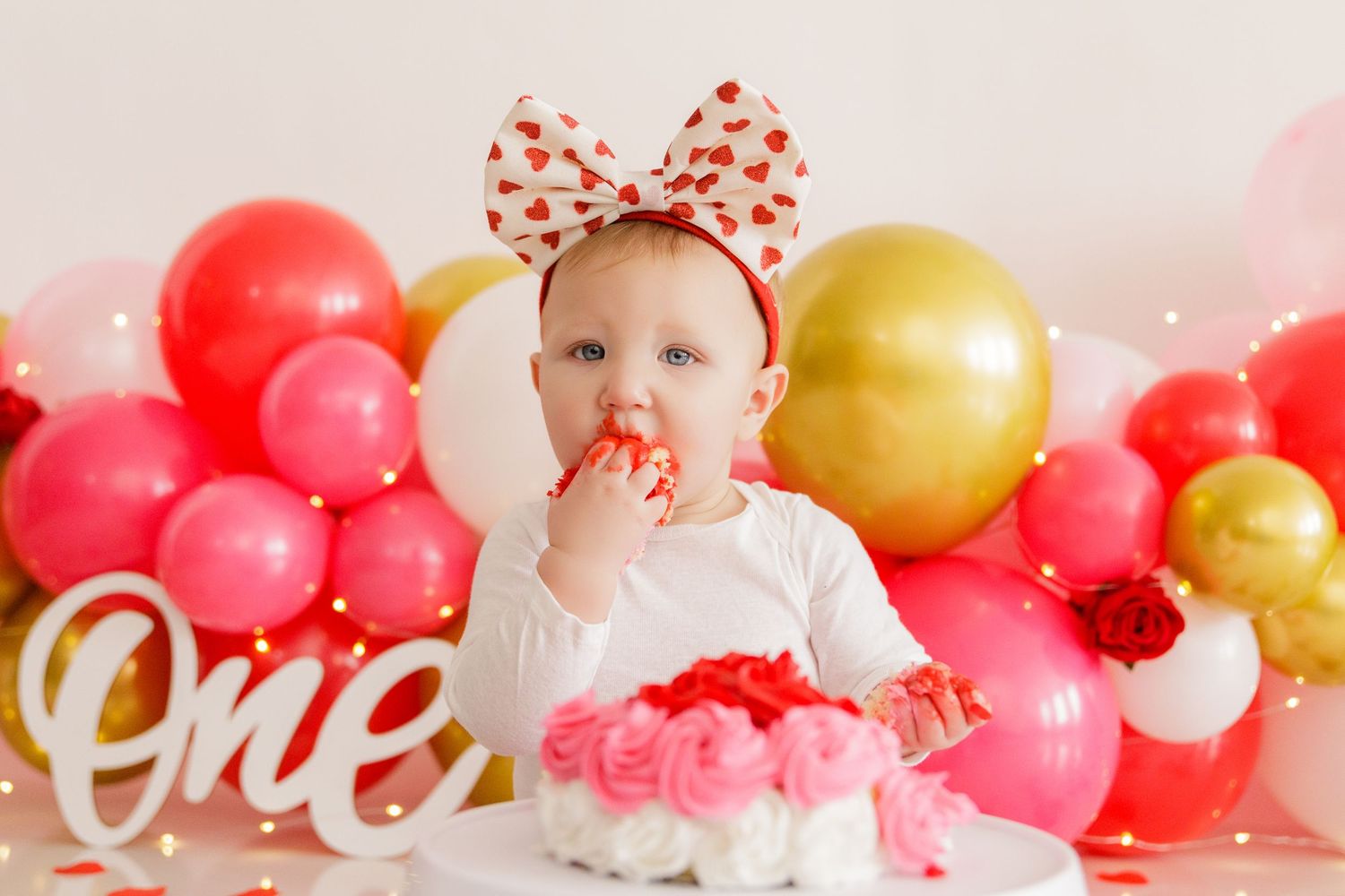Valentine's Day themed photo setup with pink and gold balloon arch and white lettering.