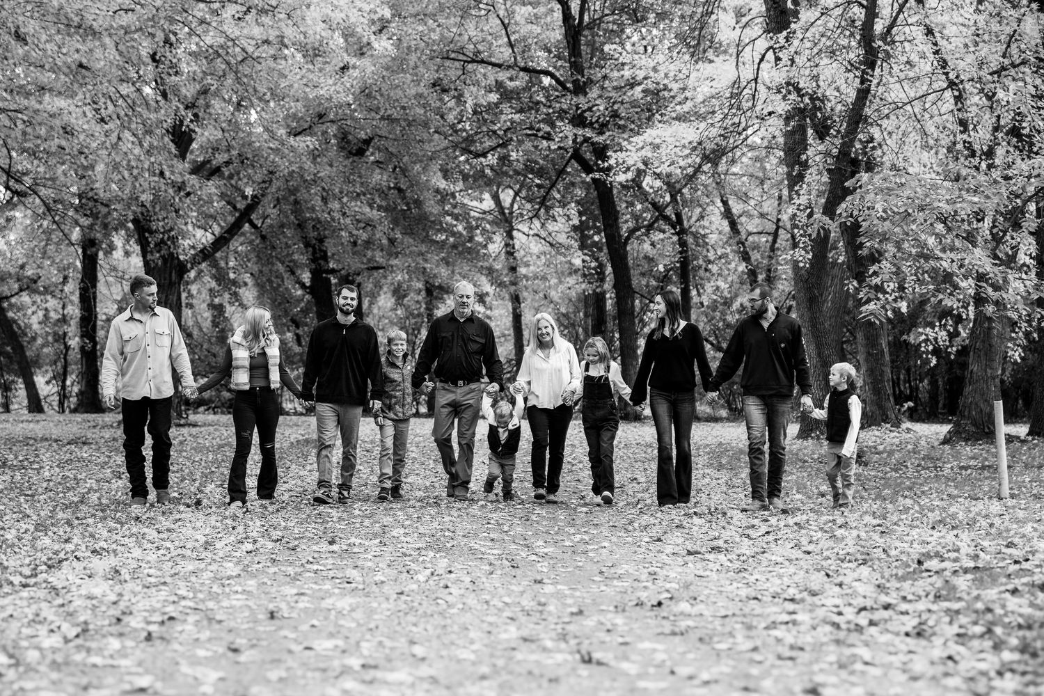 Group walking together in a line through a park with autumn leaves on the ground in black and white.