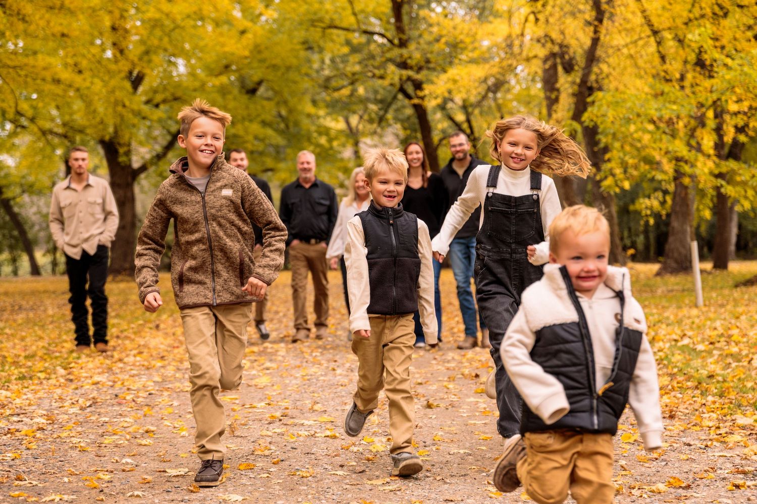 People running and playing in a line through autumn leaves in a park setting.