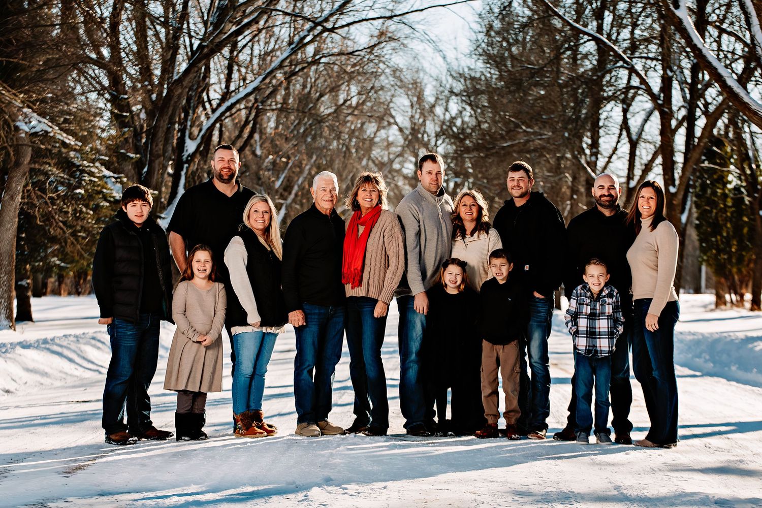 A large group poses together on a snowy winter path surrounded by bare trees in a park setting.