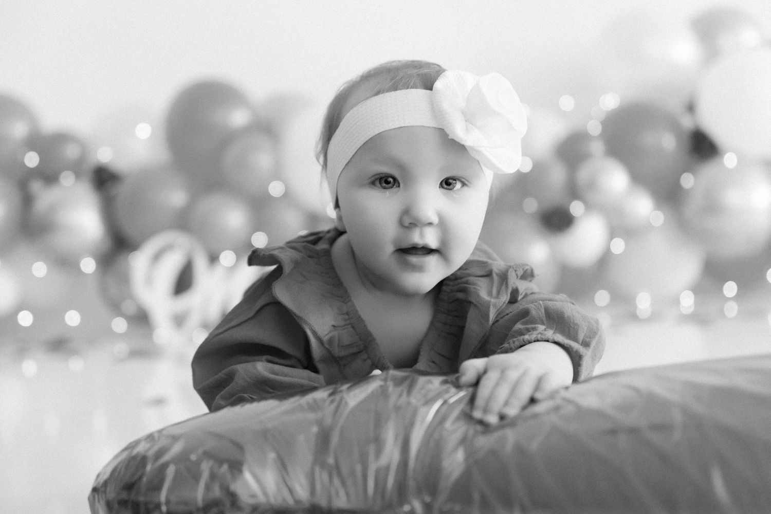 A festive first birthday cake smash setup with pink and gold balloons and decorative lighting.