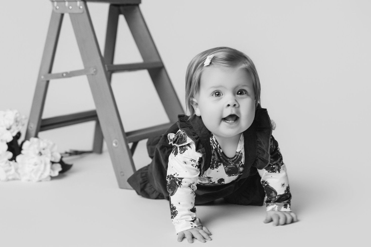 Black and white portrait series of baby crawling near wooden ladder prop.