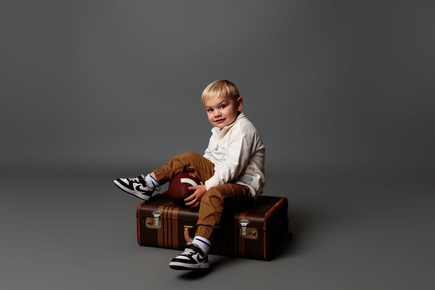 Child sitting and playing in a vintage wooden box during professional photo session.