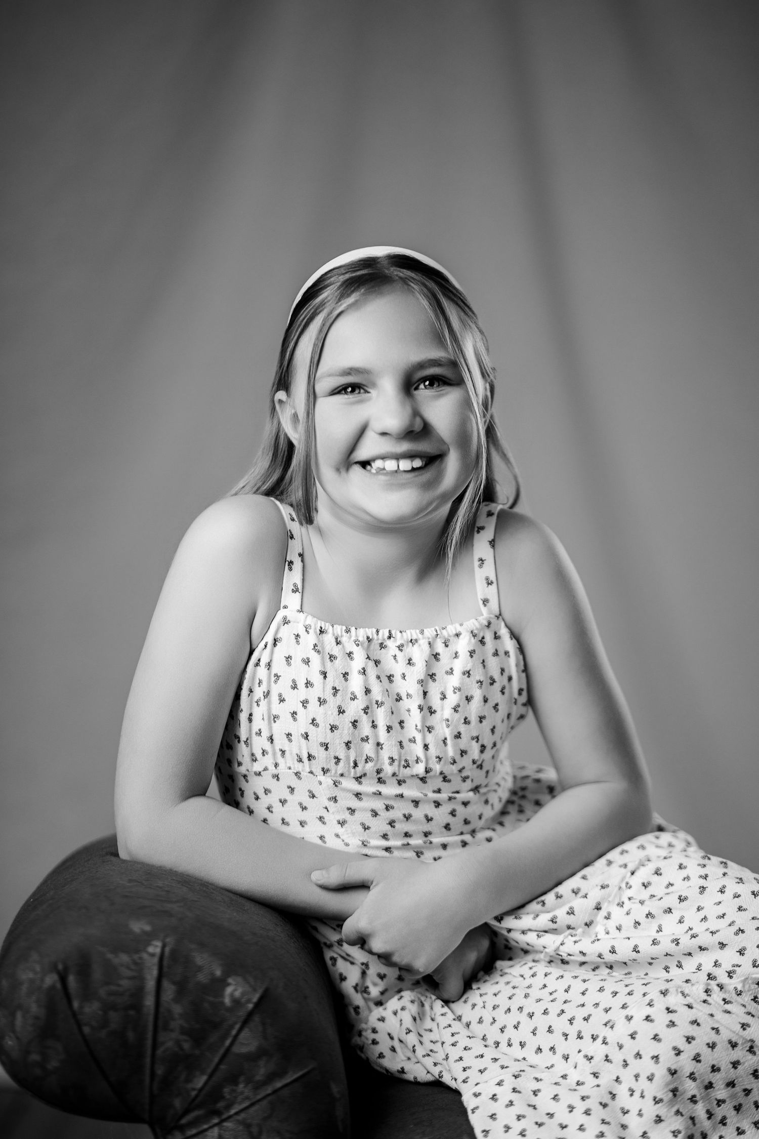 Black and white studio portrait of a laughing girl in a floral dress with a headband.