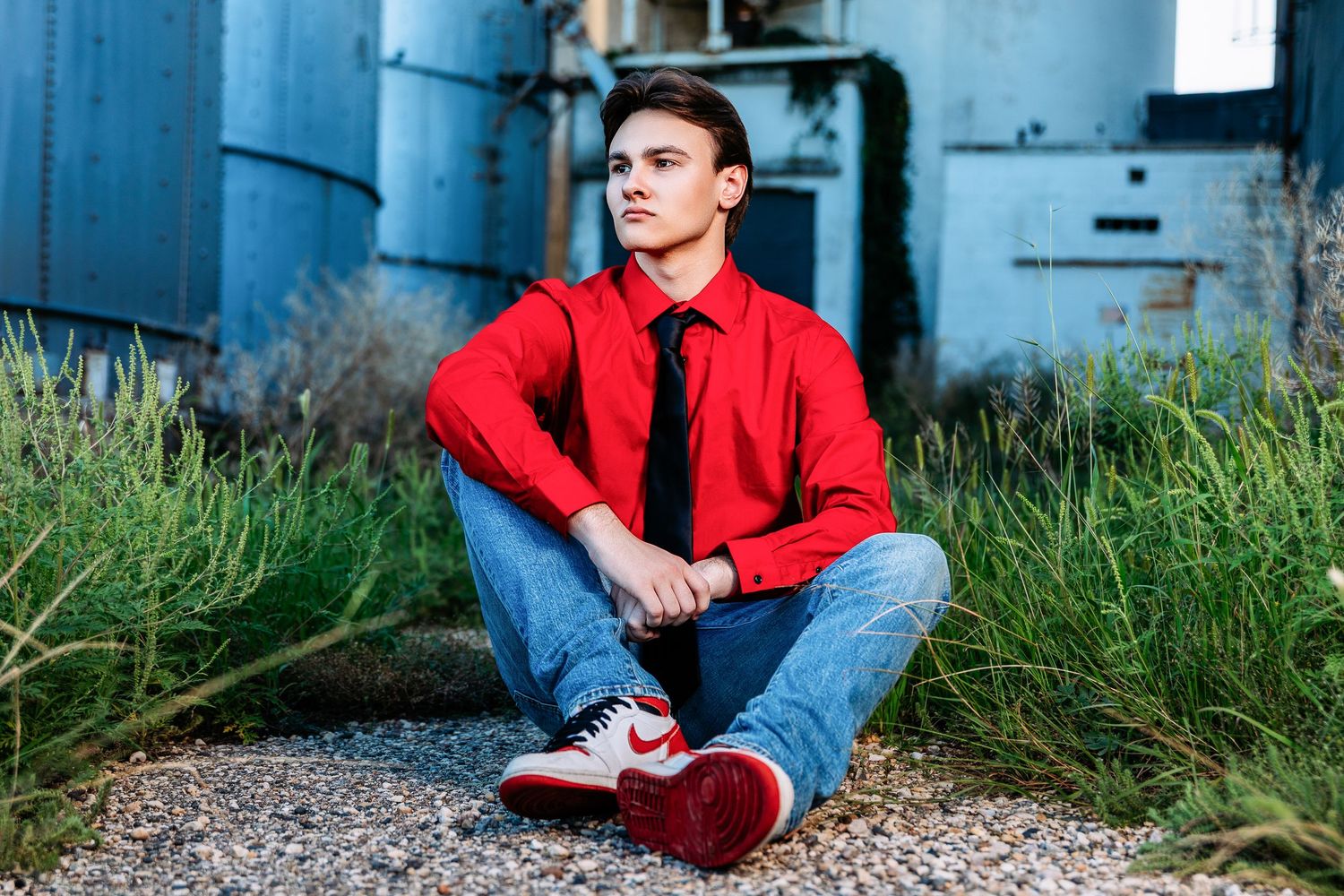 Person in red shirt and jeans sits on gravel path against blue wall in outdoor setting.