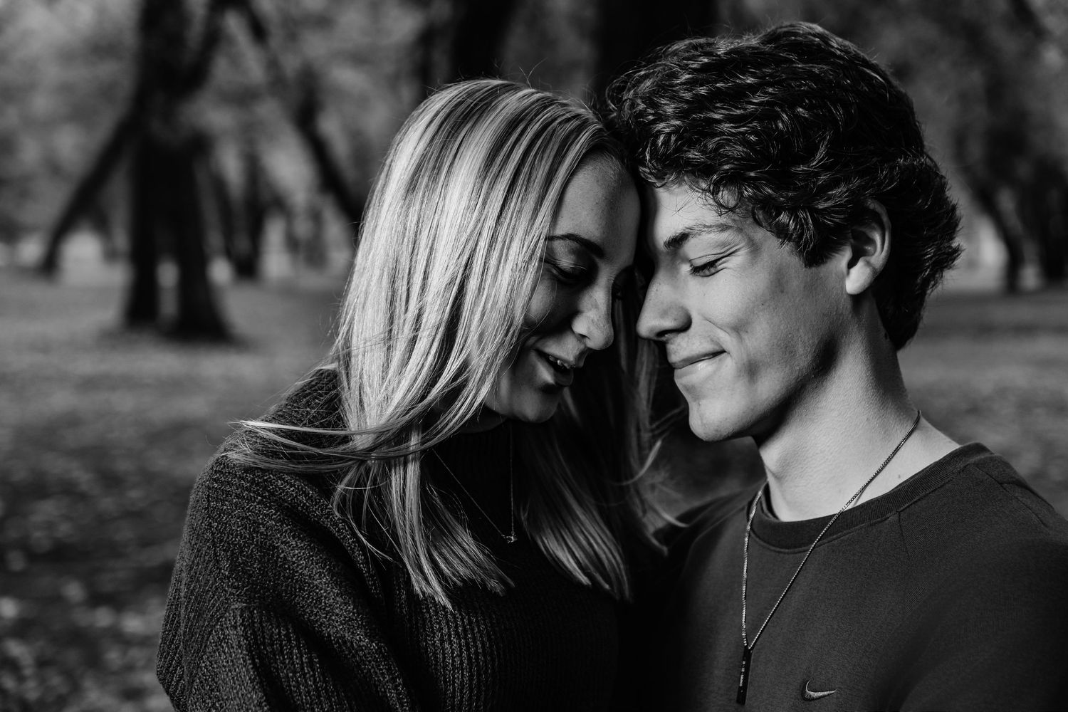 Close-up portrait of a couple leaning in close together against blurred autumn trees.