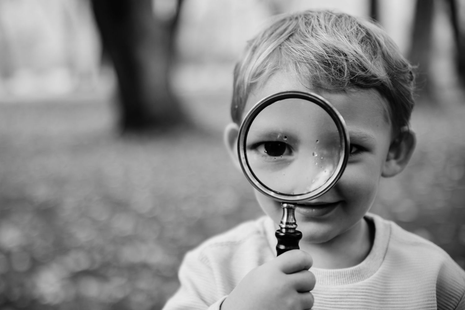 Black and white close-up of a child looking through a magnifying glass.