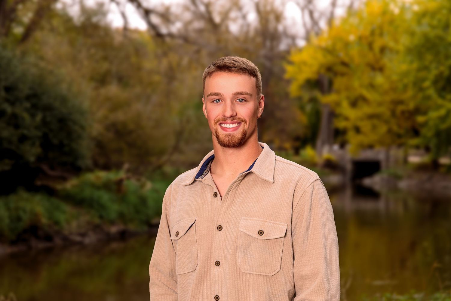 A man poses outdoors wearing a light beige button-up shirt during a fall photo session.