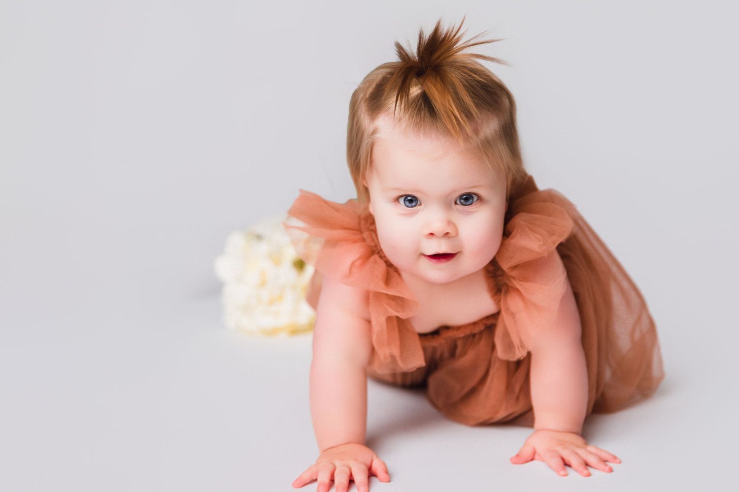 Baby in peach tulle dress crawling and exploring studio setting.