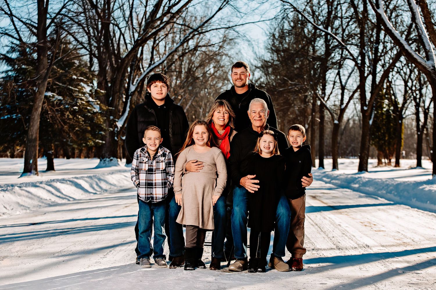 Large family gathering outdoors in a snow-covered park with winter trees creating a natural backdrop.