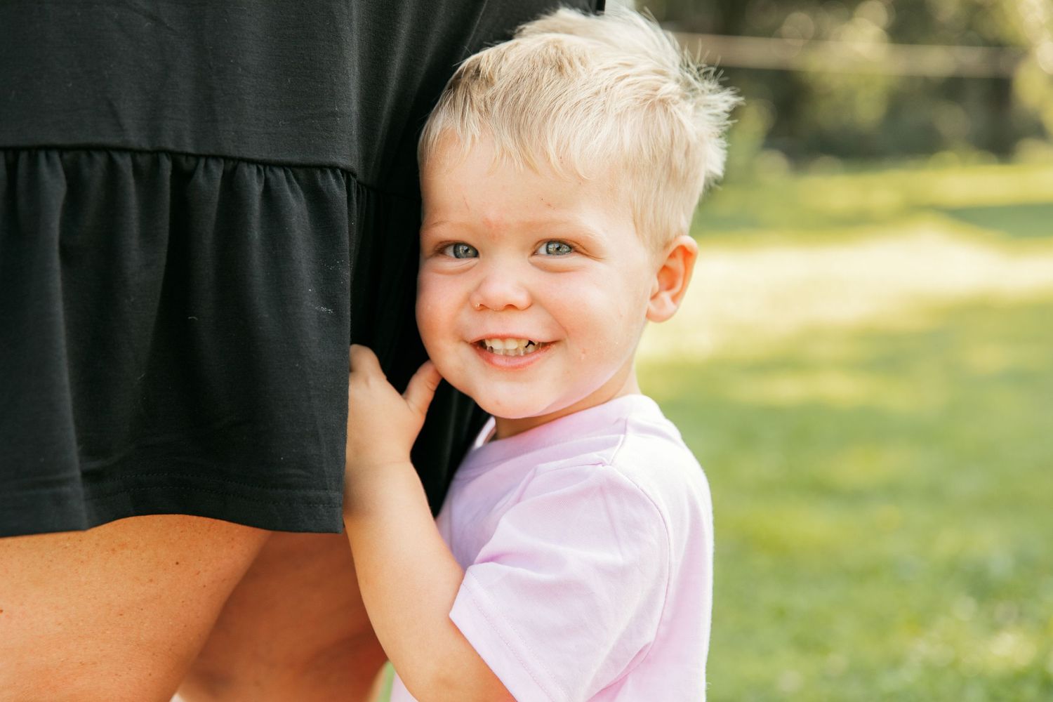 Young children in light colored clothing smile while being held against a dark background outdoors.