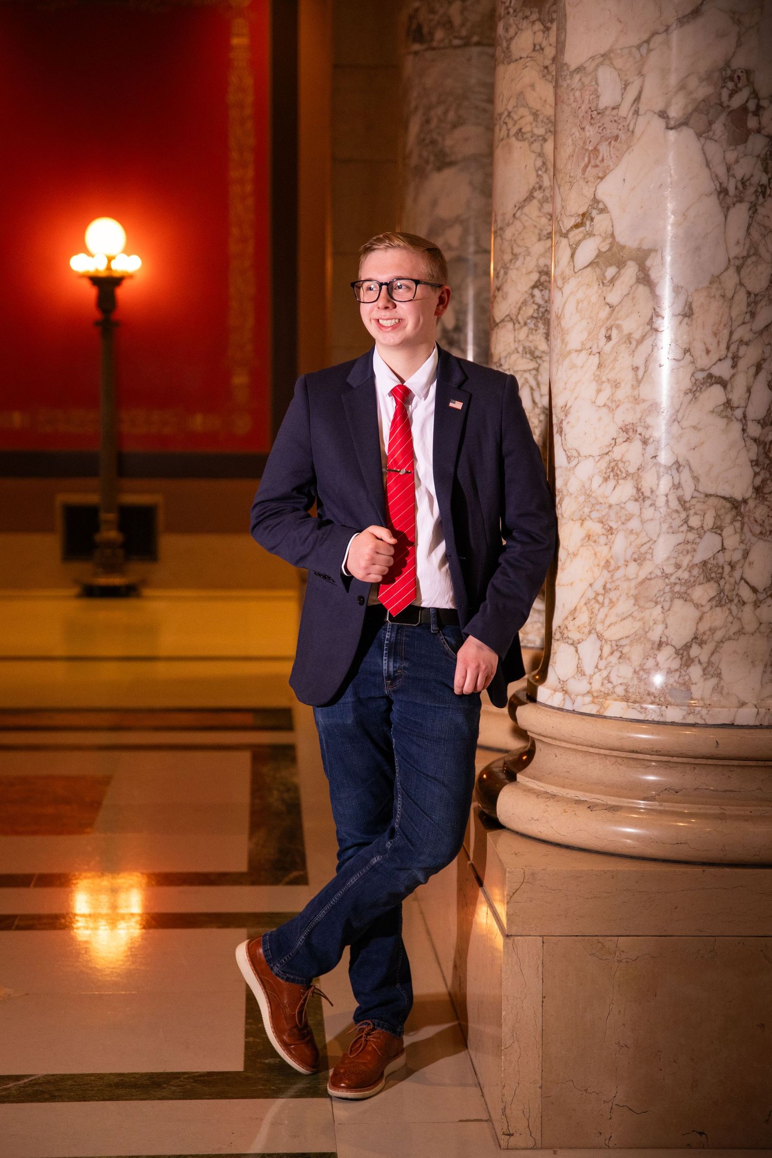 Professional portrait session in formal attire against marble columns with warm lighting in an elegant indoor setting.