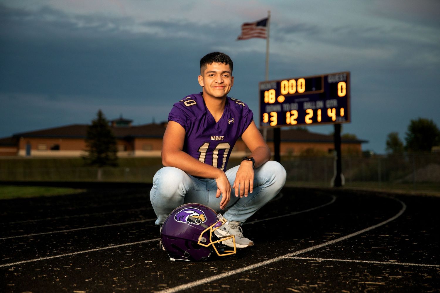 A dramatic stormy sky serves as backdrop for a football scoreboard showing 0-0 at a high school stadium.