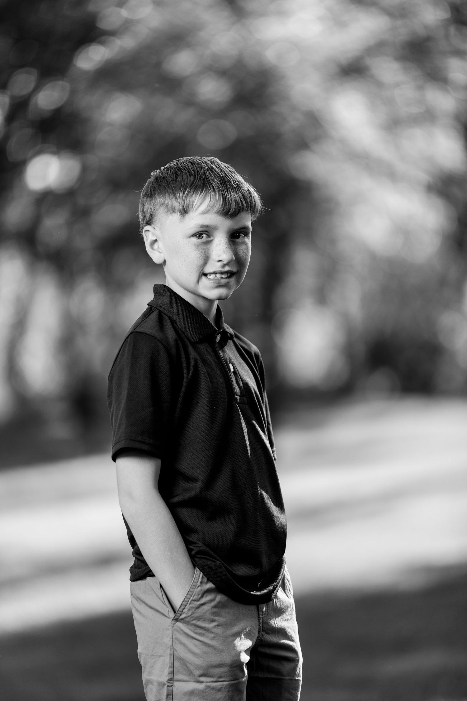 Smiling boy in black polo shirt standing outdoors in black and white portrait photo.