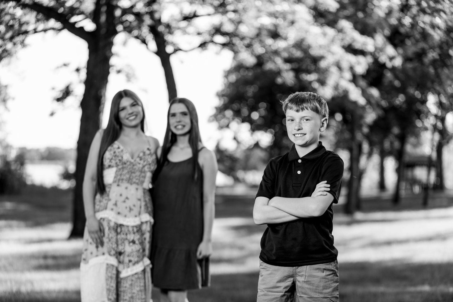 Black and white photo of two girls and a boy with arms crossed posing in a park.