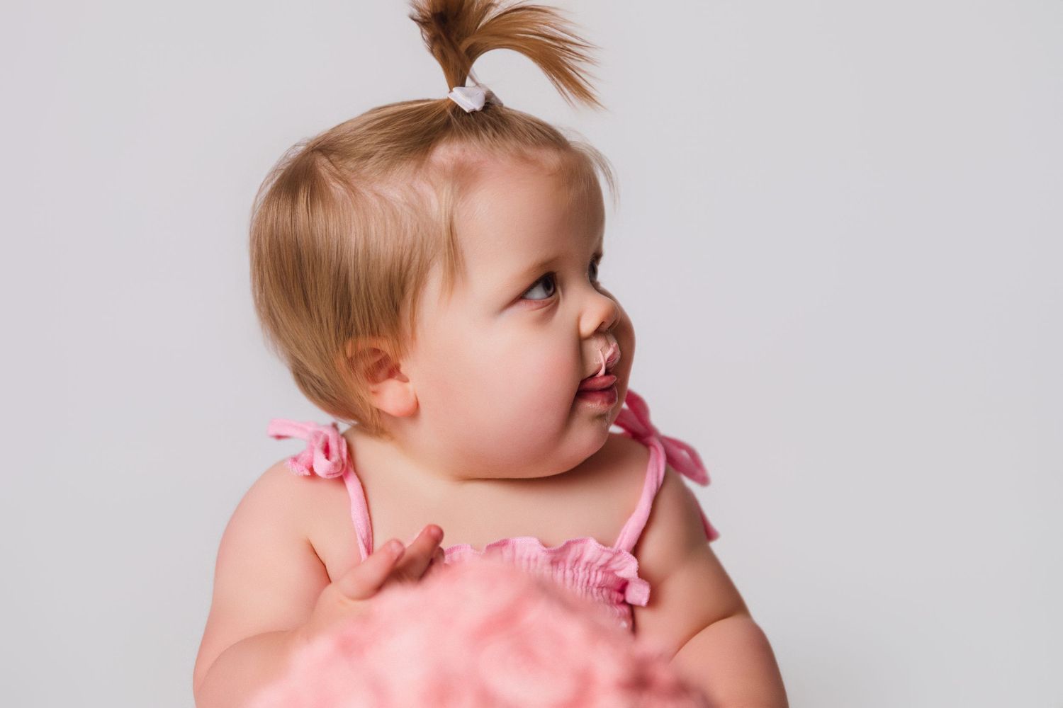 Baby in pink dress during studio photoshoot with natural lighting.