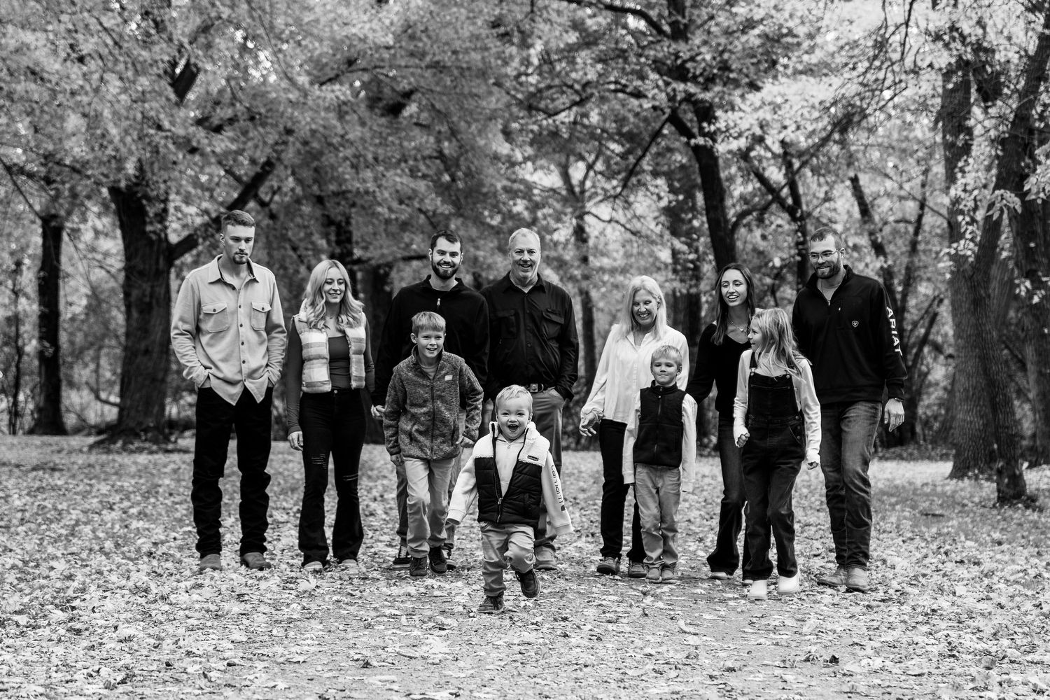 Wide black and white shot of extended family group standing among autumn trees.