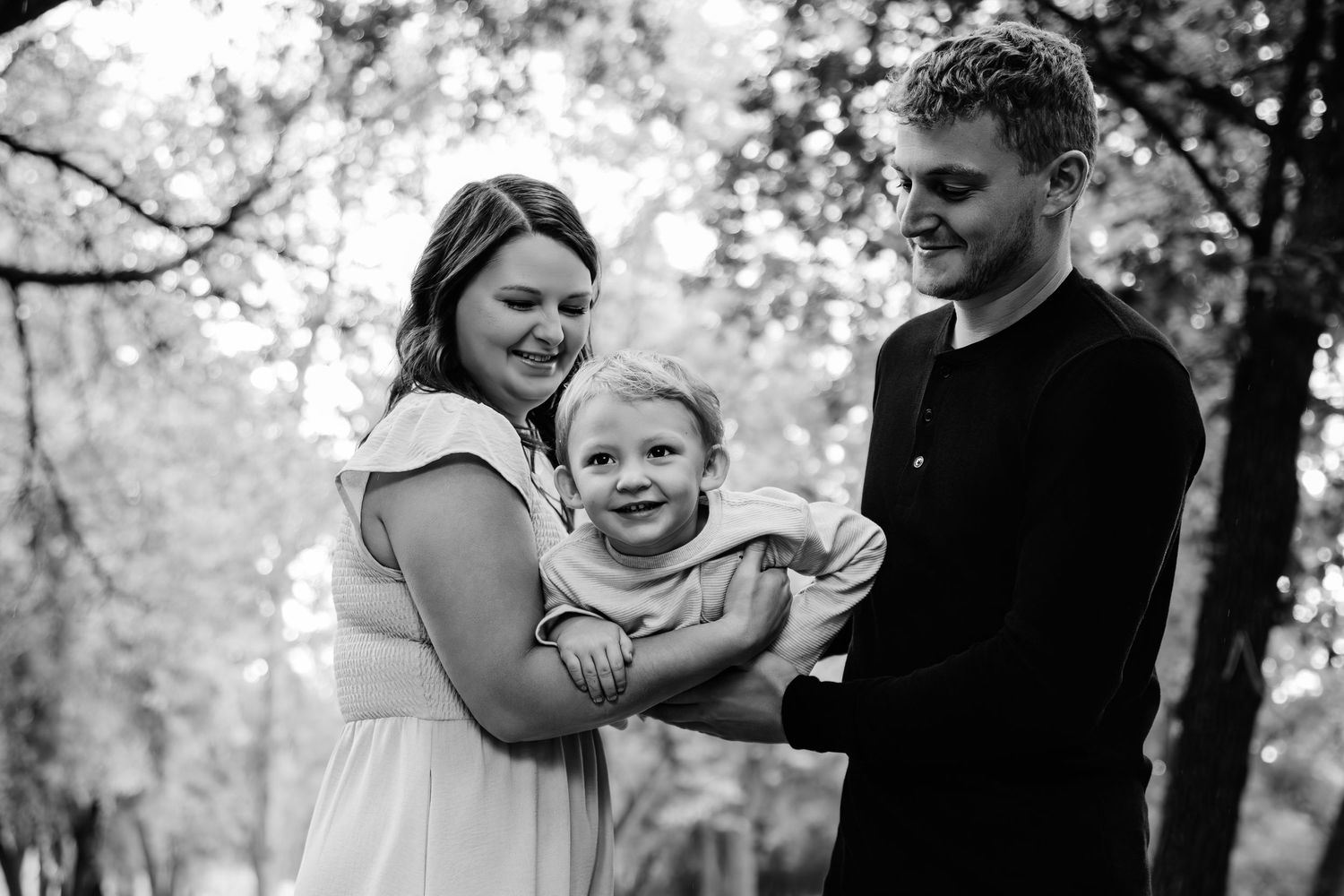 A family shares joyful moments together in black and white on a wooded path.