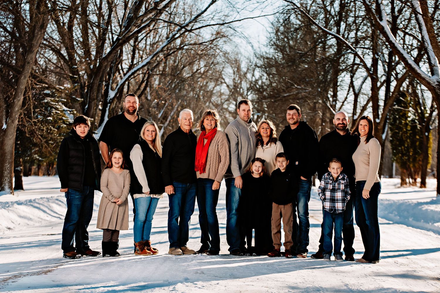 A large family group poses together on a snowy path surrounded by bare winter trees.