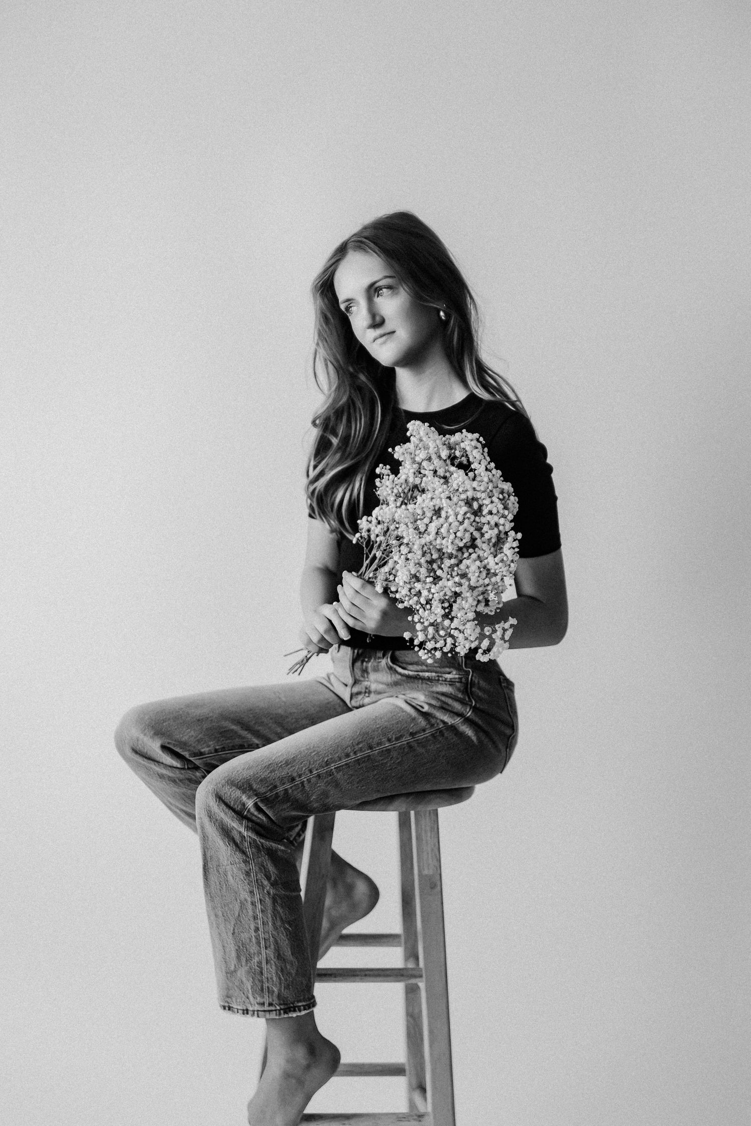 Black and white portrait of woman on stool holding bouquet of white wildflowers, jeans.