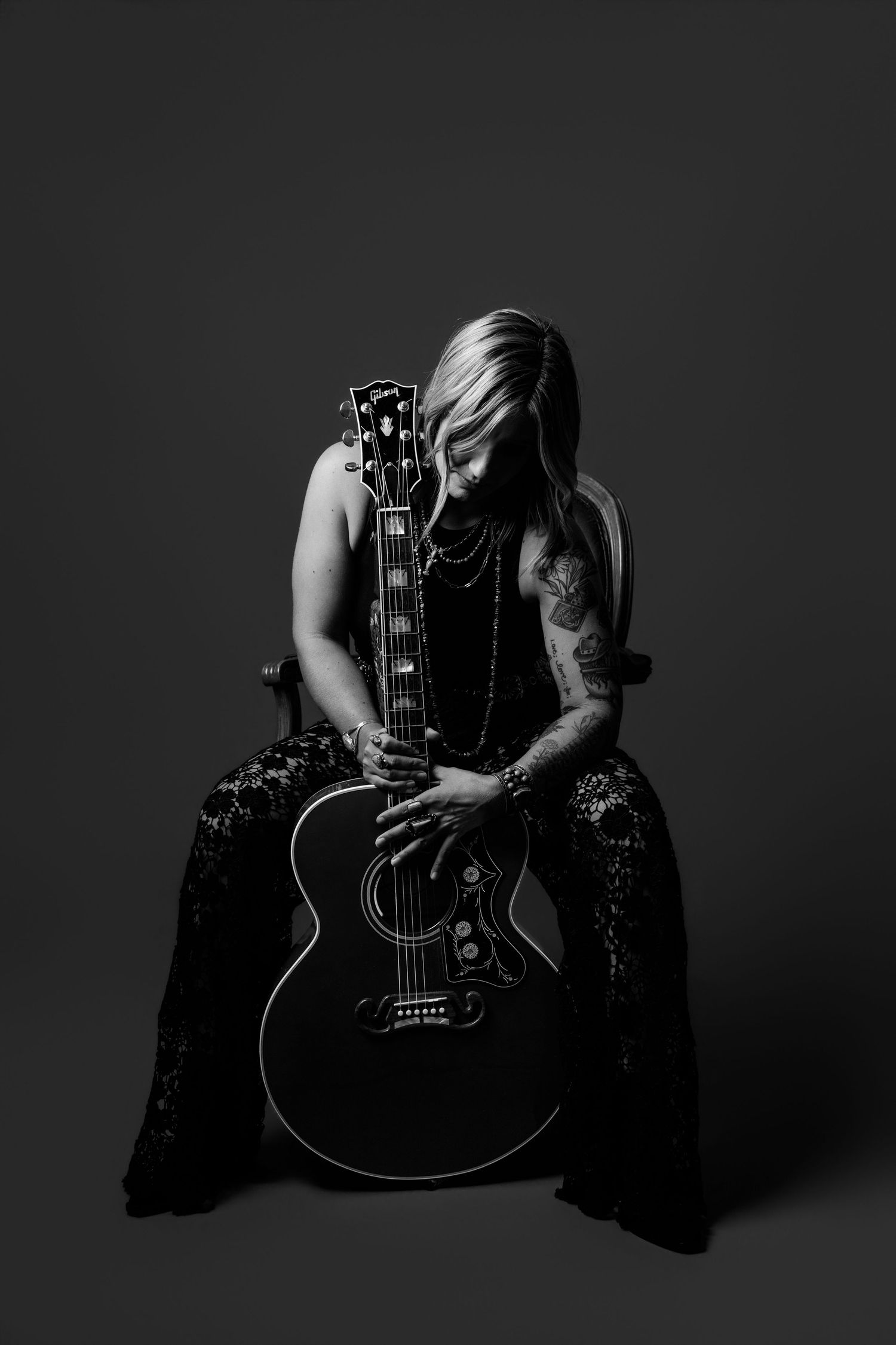 Woman in sequined outfit embracing a black acoustic guitar in moody black and white portrait.