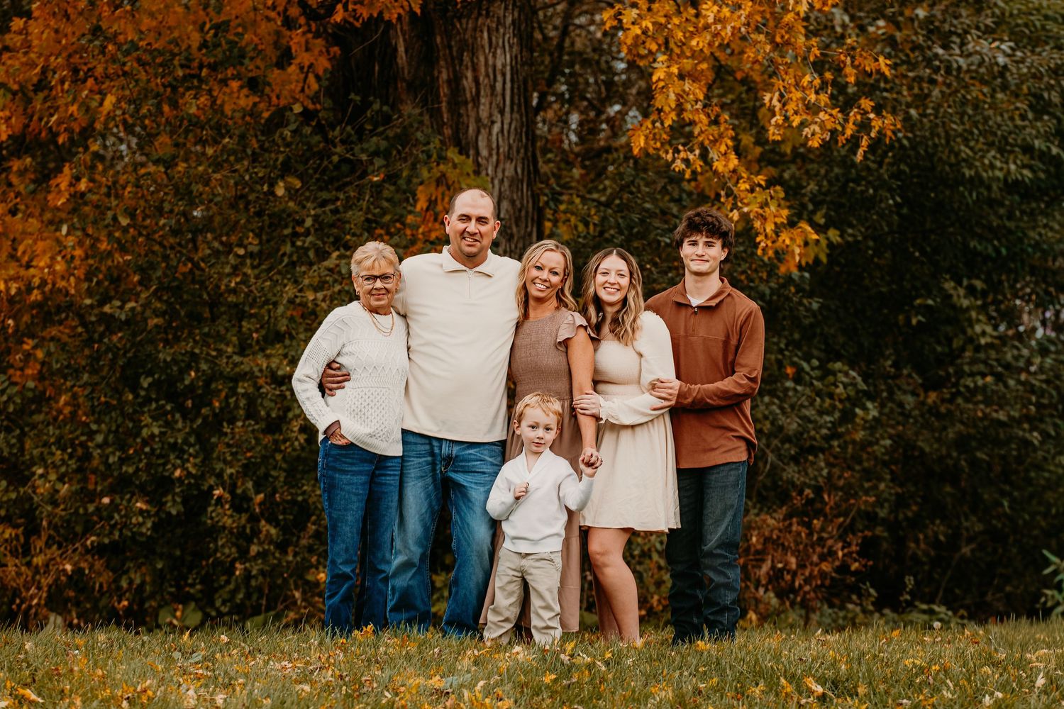 A group poses together outdoors during autumn with vibrant orange foliage in the background.