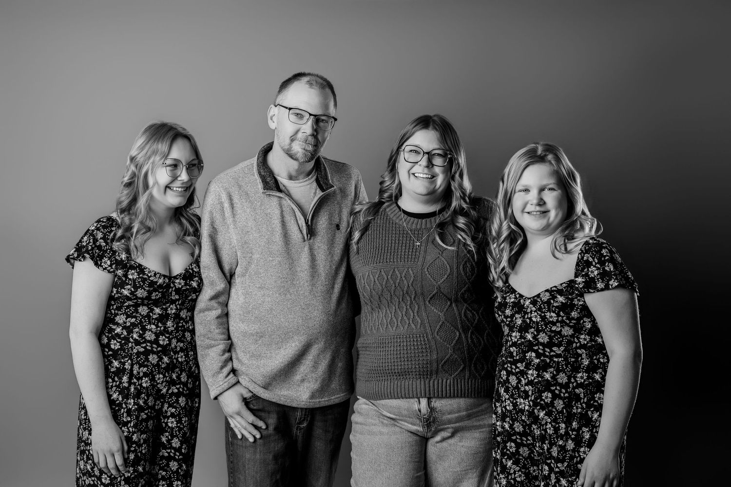 Black and white portrait of a family of four smiling together against a neutral studio background.
