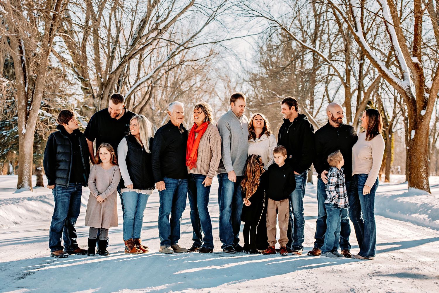 A large family group poses together on a snowy winter path surrounded by bare trees.