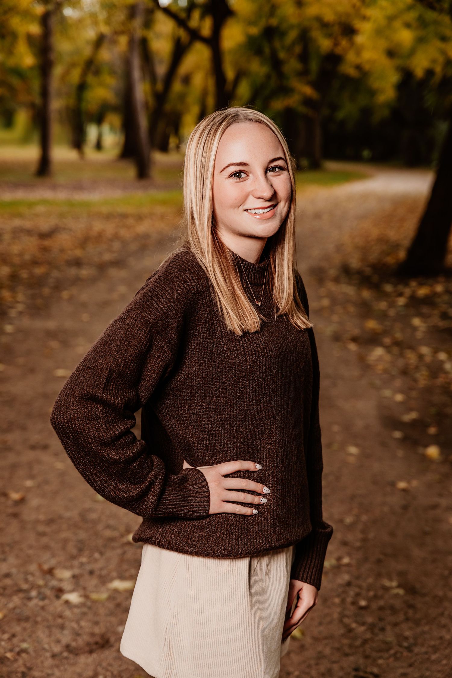Person in brown sweater poses against autumn forest backdrop.