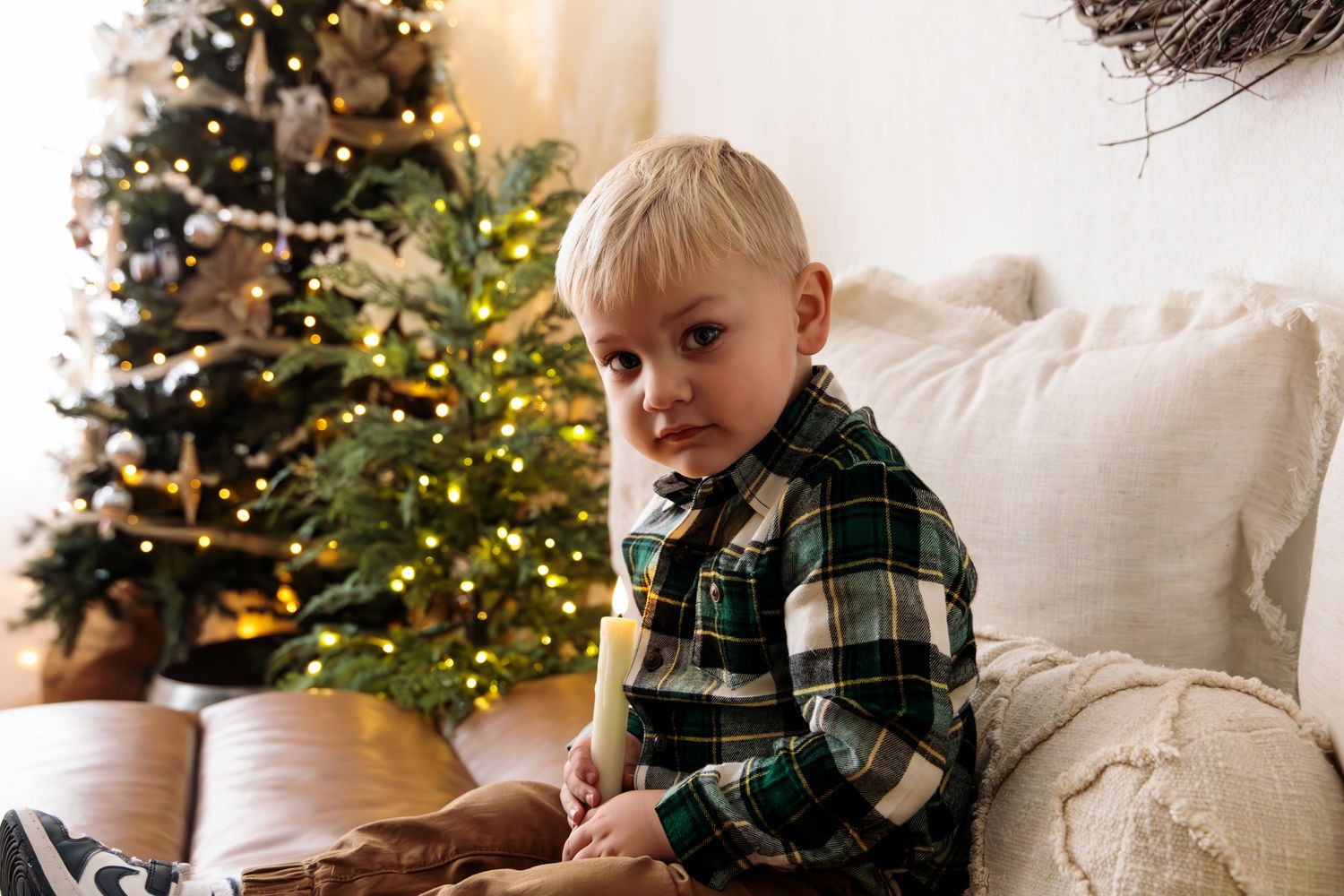 Holiday portraits of child in plaid shirt lounging on white couch near decorated Christmas tree.