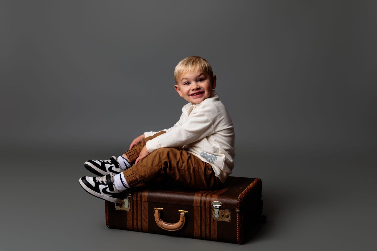 A child poses inside a vintage brown suitcase during a studio photoshoot.