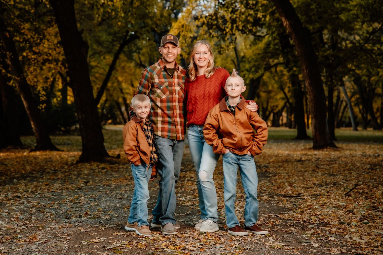 A family walks together through a park filled with fallen autumn leaves on a sunny fall day.