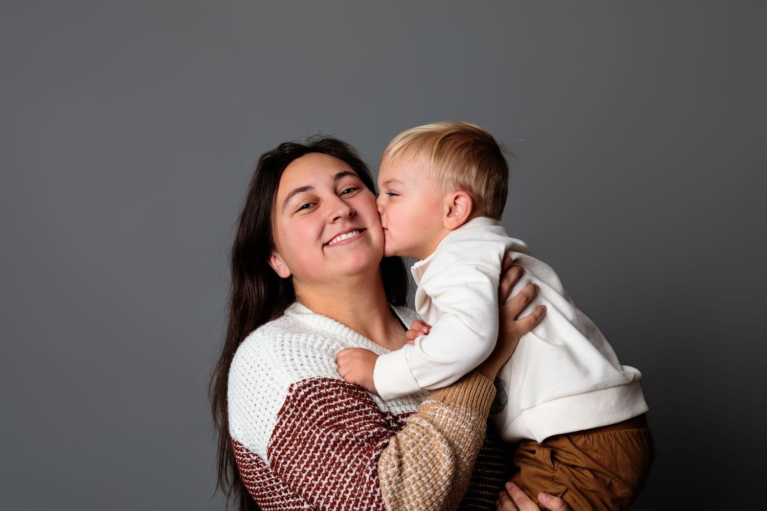 Mother and child sharing tender moment against grey studio backdrop.