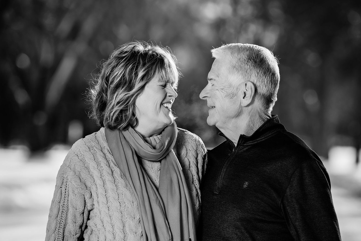 A loving couple gazes at each other in an intimate black and white portrait outdoors.