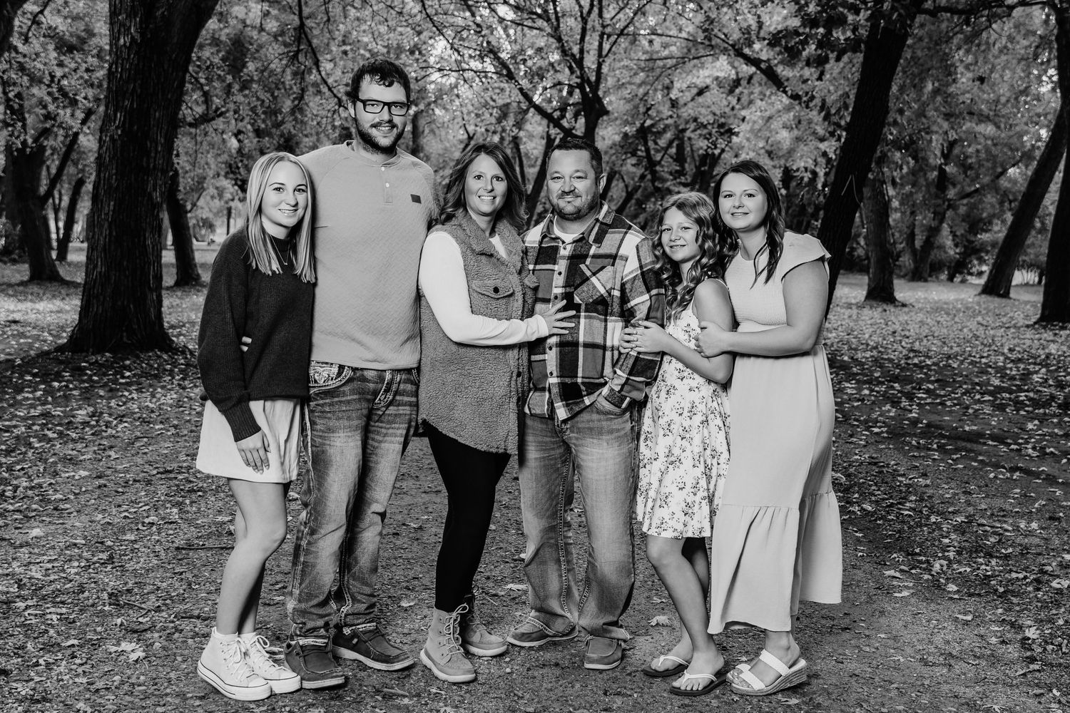 A group of people pose together outdoors in a park setting with trees in the background, captured in black and white.