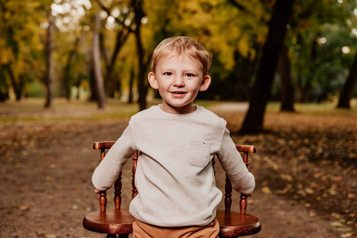 Autumn family photoshoot in a park with warm fall colors and fallen leaves on the ground.