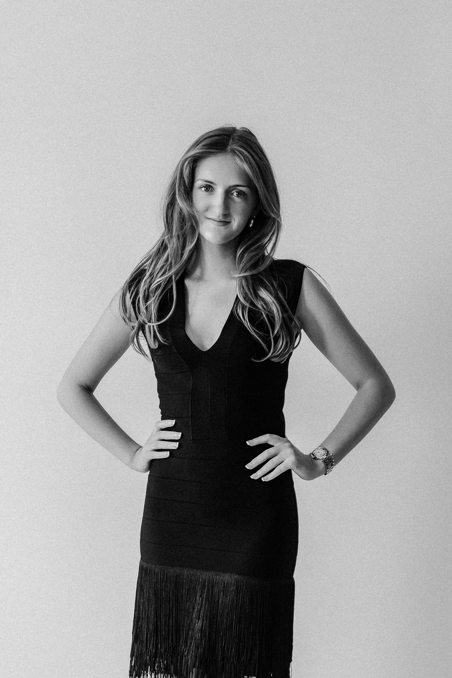 Woman in black fringe dress with hands on hips posing confidently in a black and white studio photo.