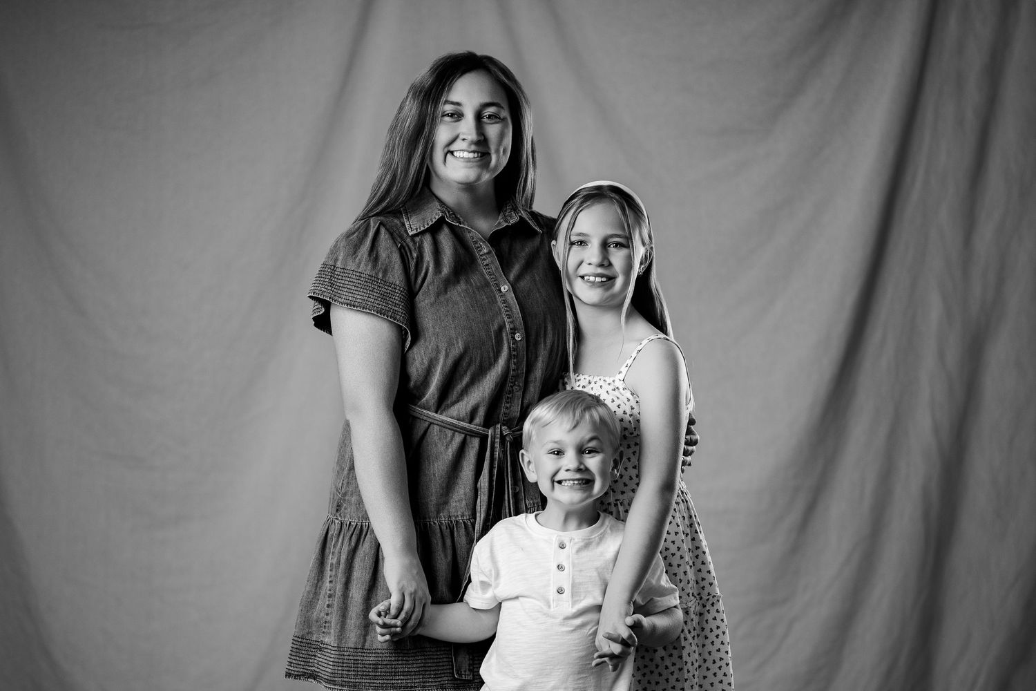 Black and white studio portrait of a woman posing with two young children against a fabric backdrop.