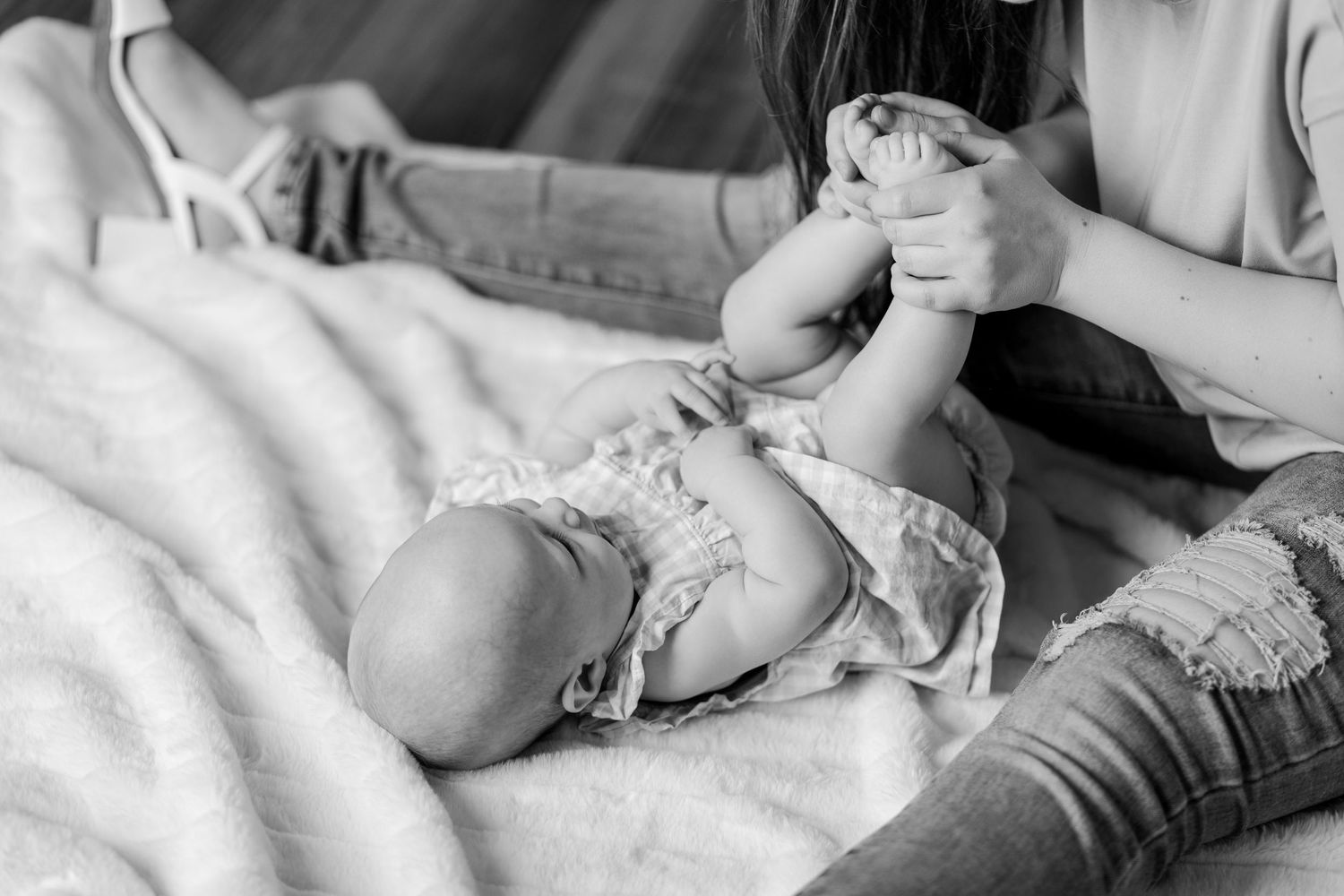 Black and white photo of mother gently holding newborn baby feet on soft blanket.