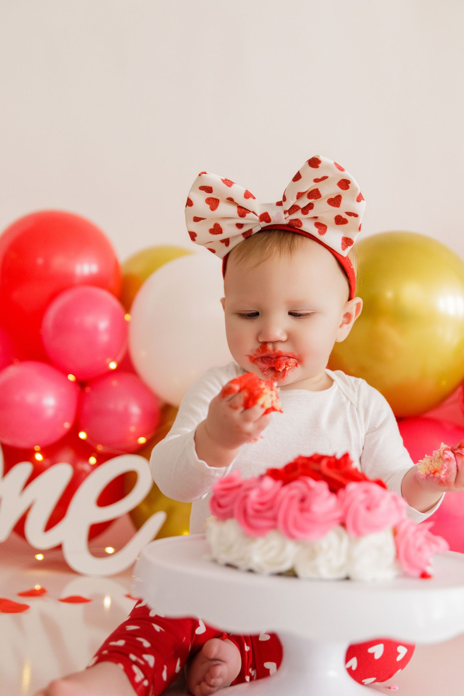 Valentine's day cake smash setup with red and white decorations and heart-patterned bow.