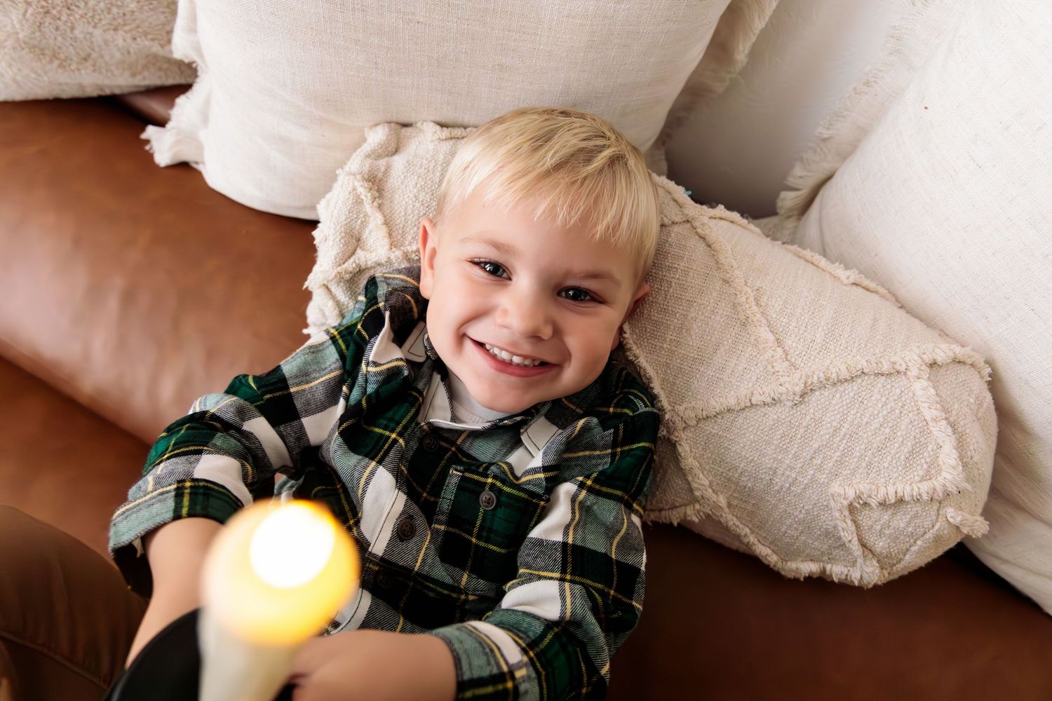 Child in plaid shirt playing with Christmas ornaments on white couch.