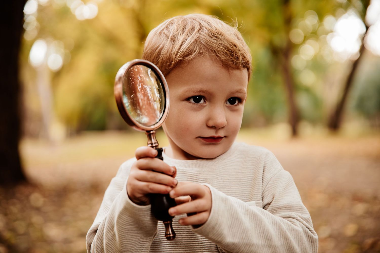 Child exploring with a magnifying glass during an autumn outdoor photo session.