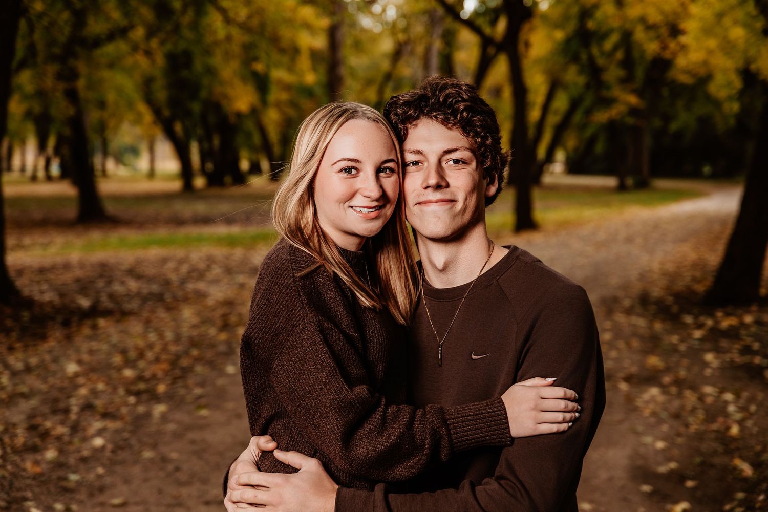 A couple embraces while wearing matching dark sweaters in an autumn park setting.