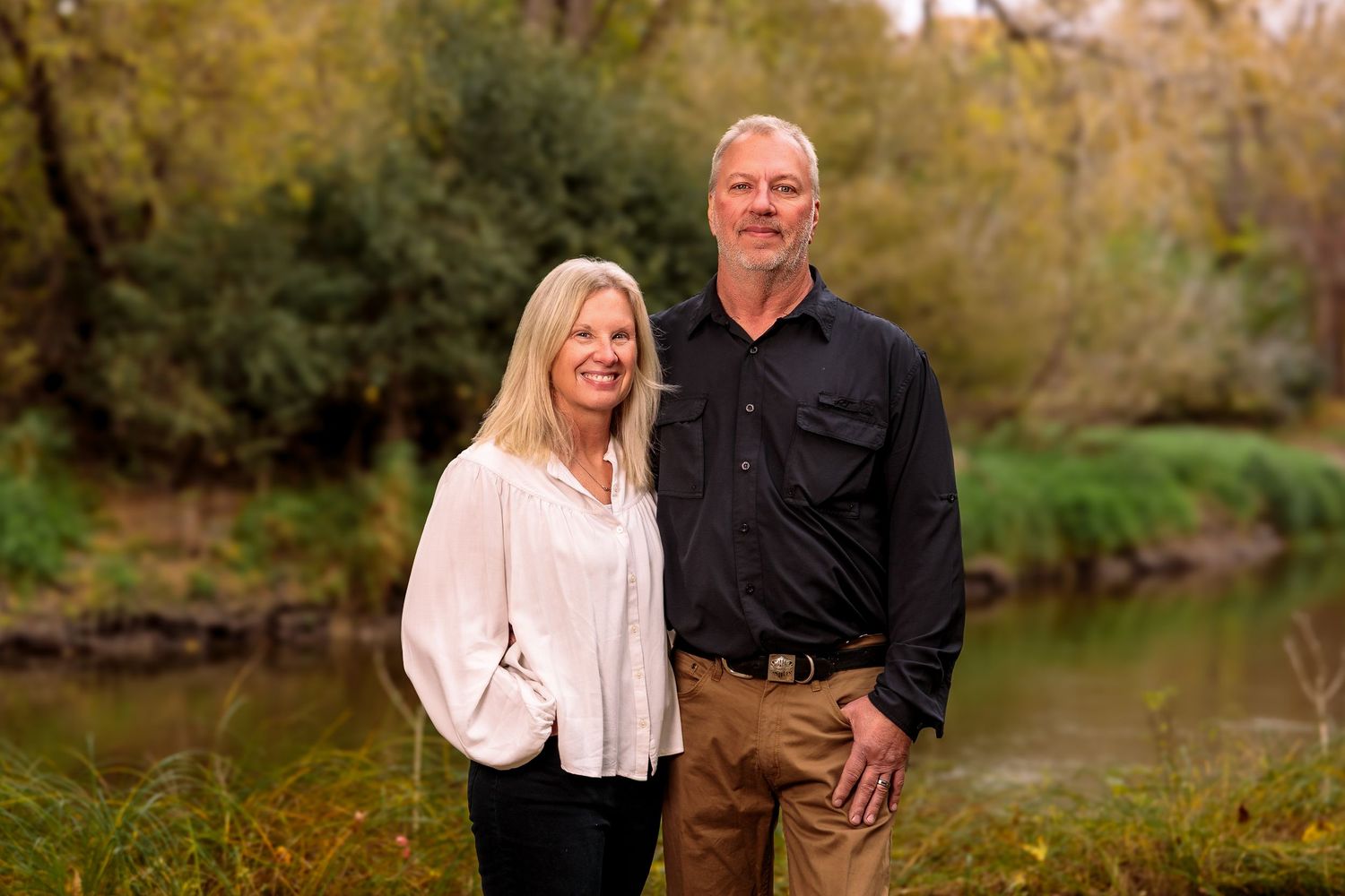 Couple standing together outdoors during a fall photo session near water.