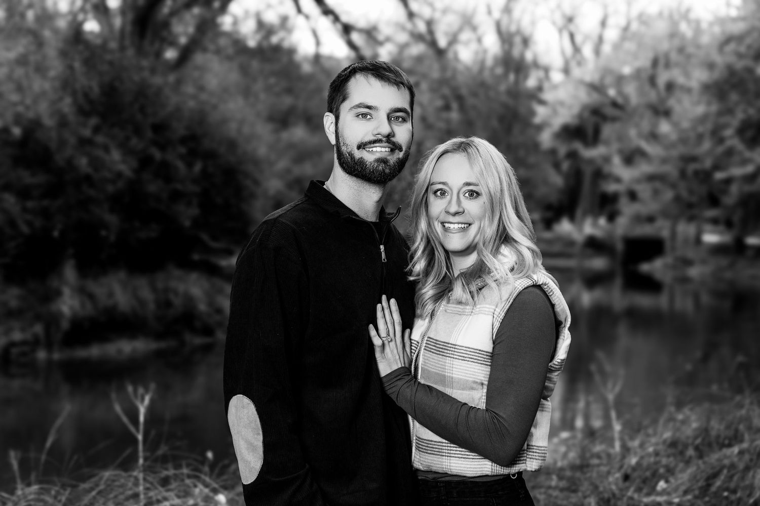 Romantic couple poses together outdoors during a fall photoshoot near a pond.